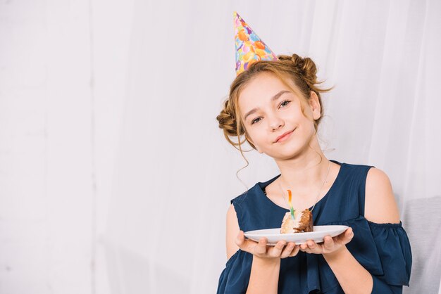 Retrato de una muchacha adolescente que lleva a cabo la rebanada de torta en la placa blanca