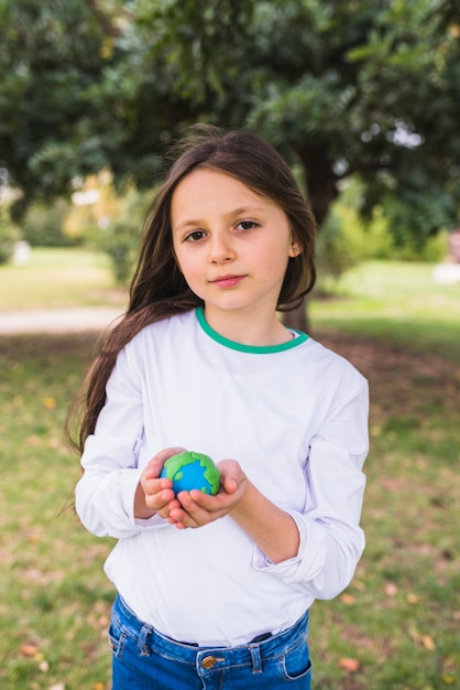 Retrato de una muchacha adorable que sostiene el mundo del planeta de la arcilla en parque