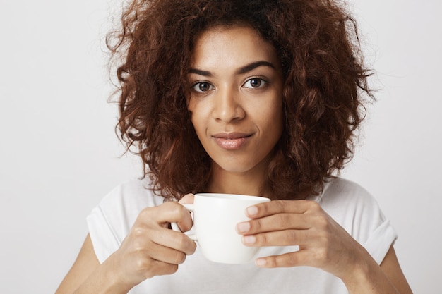 Retrato de la muchacha africana hermosa que sonríe sosteniendo la taza de café.