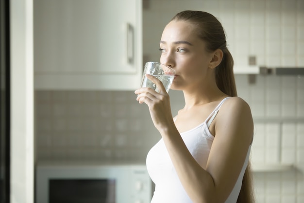 Retrato de una muchacha atractiva joven que bebe el agua