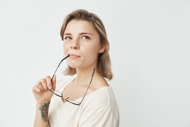 Retrato de la muchacha bonita joven que sonríe pensando soñando mordiendo los vidrios.