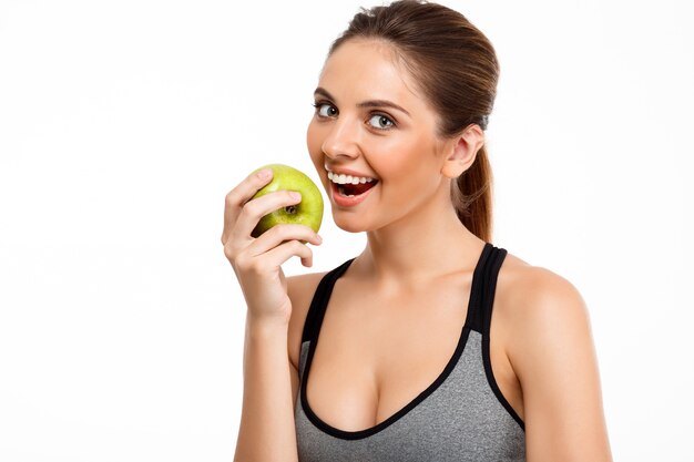 Retrato de la muchacha deportiva hermosa joven que sostiene la manzana sobre el fondo blanco.