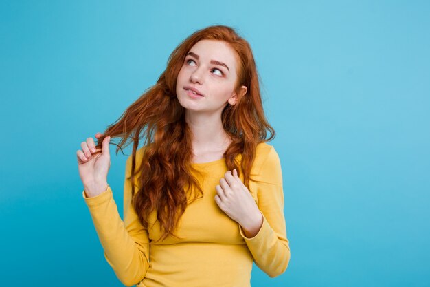 Retrato de la muchacha feliz del pelo rojo del jengibre con las pecas sonrientes que miran la cámara. Pastel de fondo azul. Espacio De La Copia.