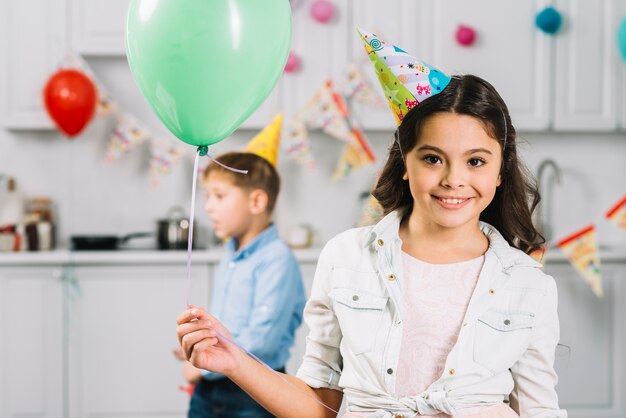 Retrato de una muchacha feliz que sostiene el globo con el muchacho que camina en fondo