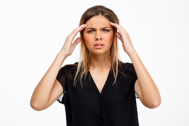 Retrato de la muchacha hermosa joven que tiene dolor de cabeza sobre el fondo blanco.