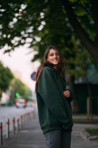 El retrato de la muchacha linda con el pelo largo mira la cámara en ciudad en fondo de la calle.