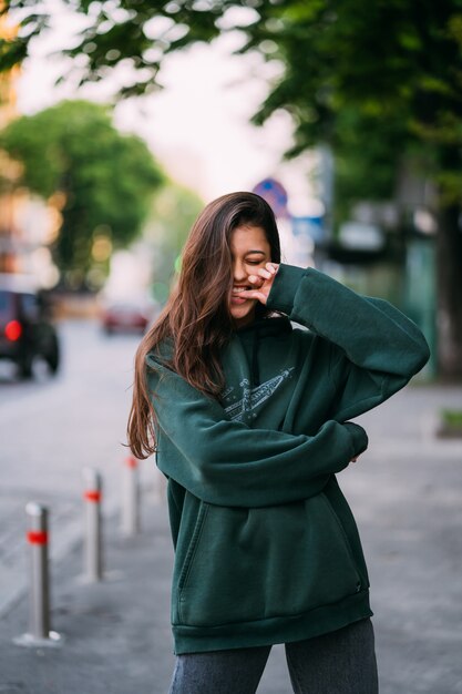 El retrato de la muchacha linda con el pelo largo mira la cámara en ciudad en fondo de la calle.