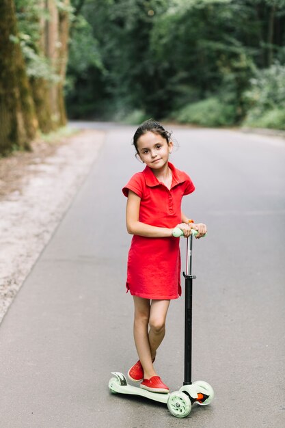 Retrato de una muchacha linda que se coloca sobre las vespas en el camino