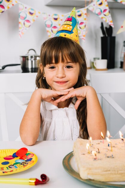 Retrato de una muchacha linda sonriente del cumpleaños con el sombrero del partido en su cabeza