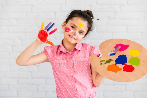 Retrato de una muchacha que muestra sus manos pintadas que sostienen la paleta coloreada multi