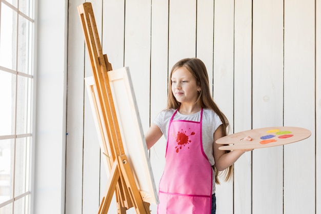 Retrato de una muchacha rubia que sostiene la pintura de madera de la paleta en el caballete