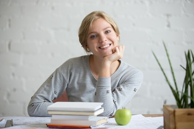 Retrato de muchacha sonriente en el escritorio con los libros y la manzana