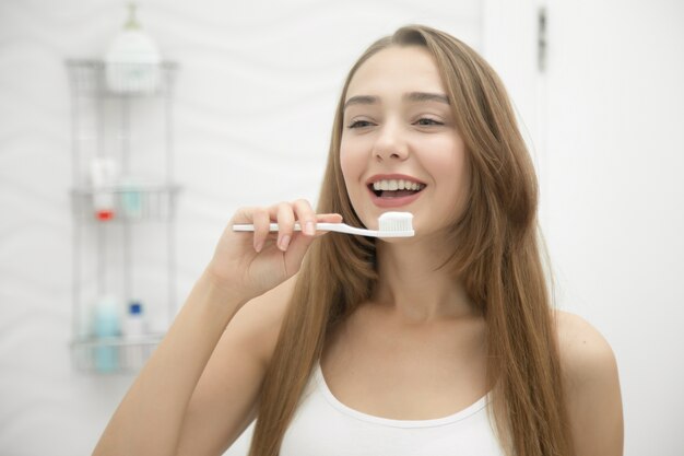 Retrato de una muchacha sonriente joven que limpia sus dientes