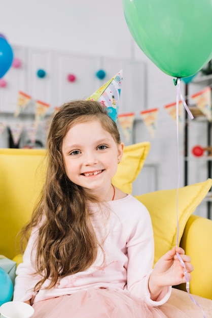 Retrato de una muchacha sonriente que se sienta en el sofá que sostiene el globo verde en su mano
