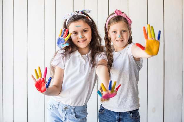 Retrato de muchachas sonrientes que llevan la venda que muestra las manos pintadas coloridas contra la pared de madera