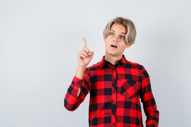 Retrato de muchacho adolescente bonito apuntando hacia arriba, mirando a otro lado con camisa a cuadros y mirando inteligente vista frontal