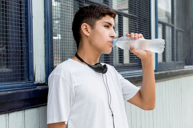 Retrato de un muchacho hermoso joven que bebe la agua fría que se coloca cerca del apartadero del hierro acanalado