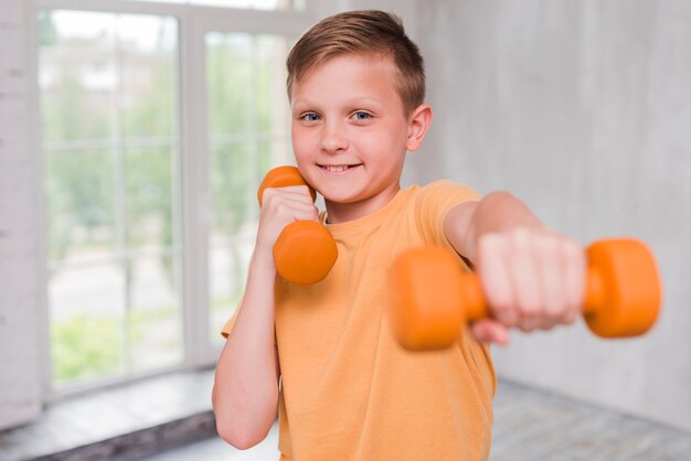 Retrato de un muchacho sonriente que ejercita con pesa de gimnasia