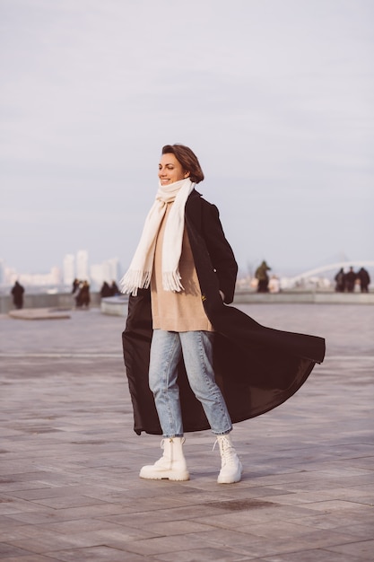 Retrato de mujer en abrigo negro de invierno y pañuelo blanco en la plaza de la ciudad.