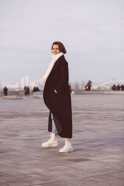 Retrato de mujer en abrigo negro de invierno y pañuelo blanco en la plaza de la ciudad.