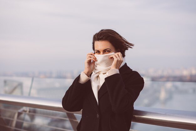 Retrato de mujer en abrigo negro de invierno y pañuelo blanco en la plaza de la ciudad.