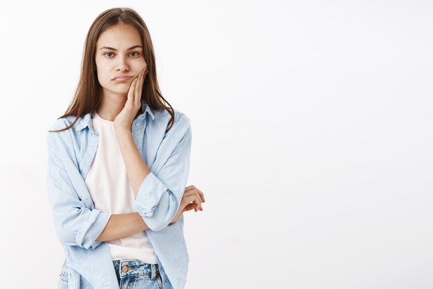 Retrato de mujer aburrida que tiene problemas para encontrar un nuevo pasatiempo sentado en casa sin nada interesante que hacer sosteniendo la mano en la mejilla mirando con indiferente mirada descuidada cruzando el pecho con un brazo