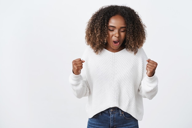 Retrato de mujer afortunada abrumada emocionada y feliz con el pelo rizado apretando los puños de triunfo y alegría gritando sí celebrando la victoria y la victoria