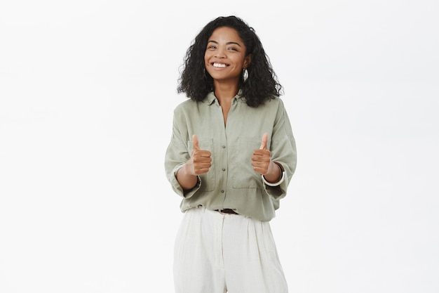 Retrato de mujer afroamericana carismática divertida y entretenida con peinado rizado mostrando los pulgares para arriba