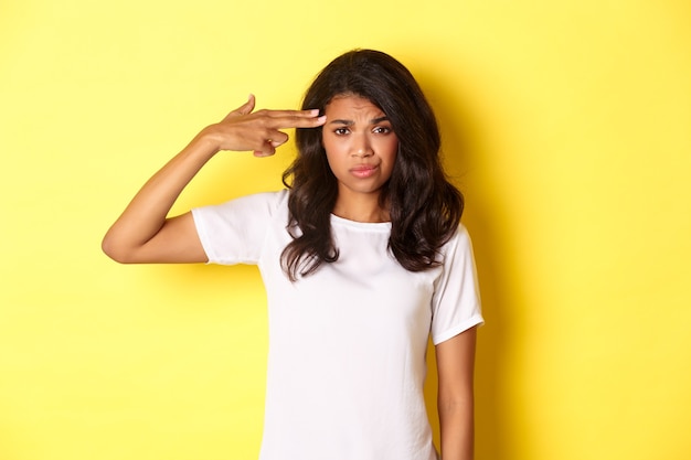 Retrato de mujer afroamericana escéptica y molesta haciendo signo de pistola de dedo sobre la cabeza