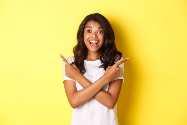 Retrato de mujer afroamericana feliz y sorprendida que muestra dos ofertas promocionales señalando con el dedo