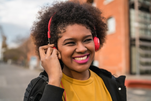 Retrato de mujer afroamericana sonriendo y escuchando música con auriculares en la calle. Al aire libre.