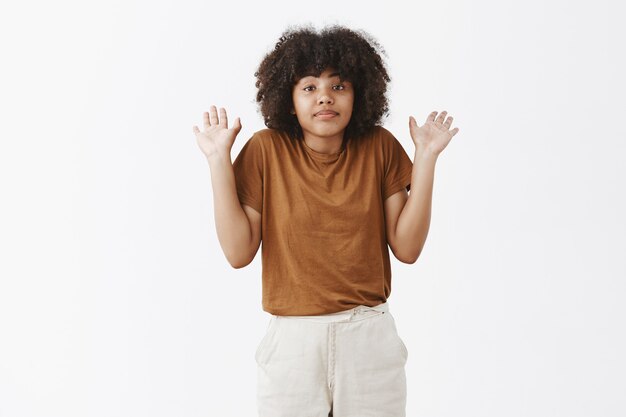 Retrato de mujer afroamericana tranquila y desinteresada no involucrada con cabello rizado encogiéndose de hombros con las palmas levantadas sin tener idea sobre el tema