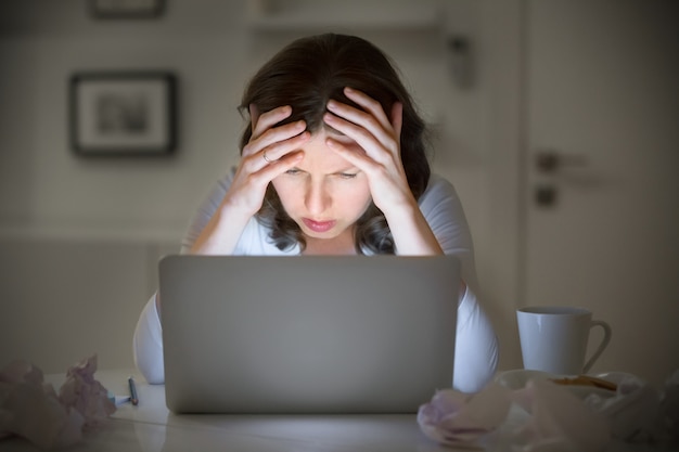 Retrato de una mujer agarrando la cabeza cerca de la computadora portátil