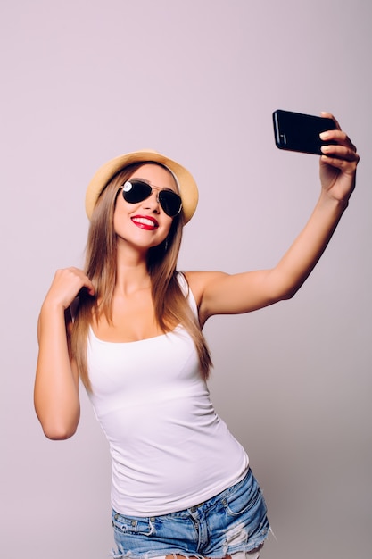 Retrato de una mujer alegre haciendo foto selfie sobre pared gris