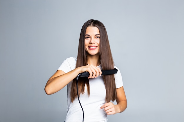 Retrato de mujer alegre con plancha para el cabello rizado preparándose para evento fecha vacaciones cómodo peinado fácil aislado en gris