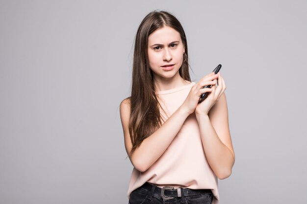 Retrato de una mujer alegre que cubre el micrófono en el teléfono inteligente aislado en una pared gris