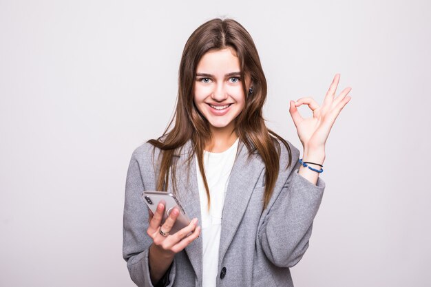 Retrato de una mujer alegre que sostiene el teléfono móvil de la pantalla en blanco mientras está de pie y mostrando gesto bien aislado sobre fondo blanco.