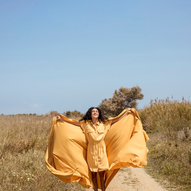 Retrato de mujer alegre con tela amarilla en la naturaleza