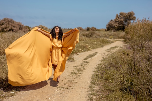 Retrato de mujer alegre con tela amarilla en la naturaleza