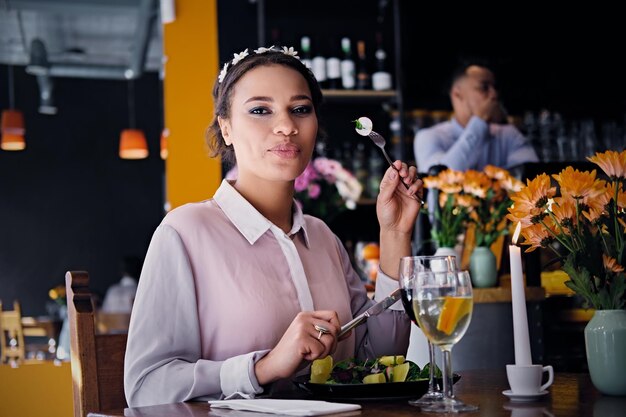 Retrato de una mujer americana negra come comida vegetariana gourmet y bebe vino en un restaurante