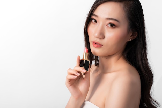 Retrato de mujer asiática de belleza atractiva en moda posando con lápiz labial con vestido blanco sobre fondo blanco para medios cosméticos o de salud