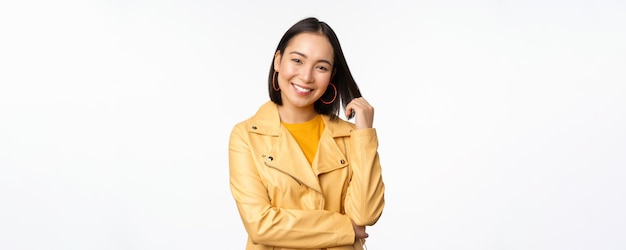 Retrato de mujer asiática con chaqueta amarilla sonriendo y luciendo feliz de pie sobre fondo blanco Copiar espacio