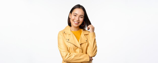 Retrato de mujer asiática con chaqueta amarilla sonriendo y luciendo feliz de pie sobre fondo blanco Copiar espacio