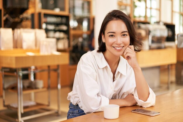 Retrato de mujer asiática confiada sentada en un teléfono inteligente de café y café en la mesa empresaria smili