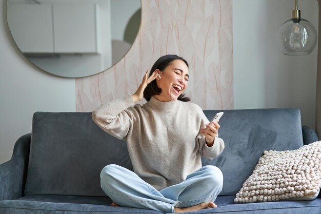 Retrato de una mujer asiática despreocupada cantando y escuchando música desde una aplicación de teléfono inteligente usando un cabezal inalámbrico