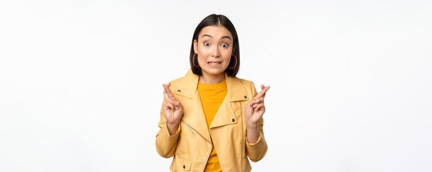 Retrato de una mujer asiática emocionada parece esperanzada deseando orar o rogar esperando noticias de pie sobre fondo blanco sonriendo entusiasta