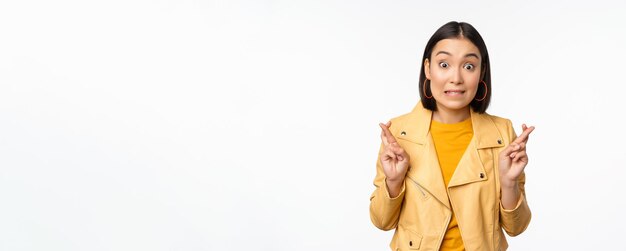 Retrato de una mujer asiática emocionada parece esperanzada deseando orar o rogar esperando noticias de pie sobre fondo blanco sonriendo entusiasta