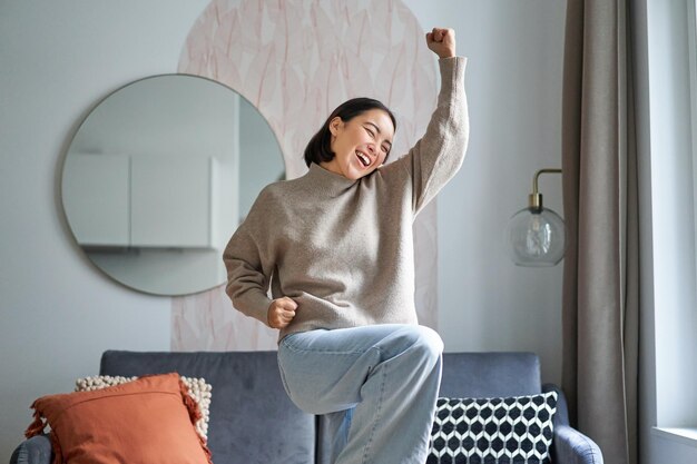 Retrato de mujer asiática feliz bailando regocijándose y triunfando sintiéndose optimista en casa