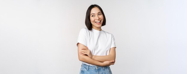 Retrato de una mujer asiática feliz sonriendo posando con los brazos cruzados confiados en el pecho de pie contra el fondo del estudio