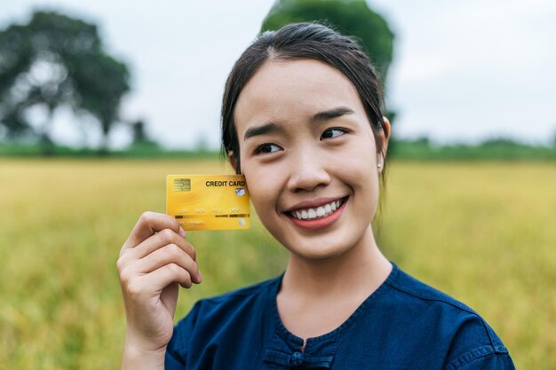 Retrato de mujer asiática joven agricultor mostrando tarjeta de crédito en campo de arroz